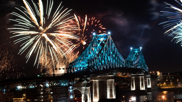 Une photo montrant le pont Jacques-Cartier illuminé en turquoise pendant que des feux d'artifice explosent en arrière-plan.