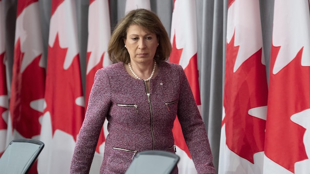 Mona Nemer marche devant des drapeaux du Canada.