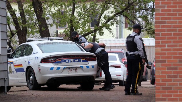 Trois policiers à côté d'une voiture de patrouille durant une intervention.