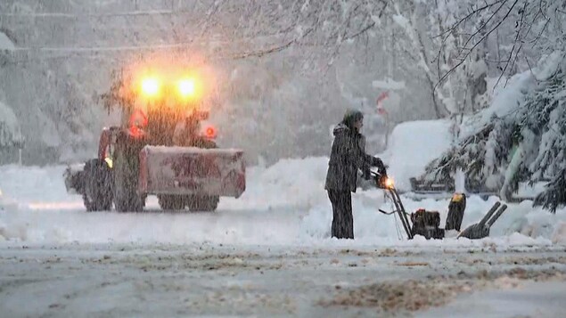 Un homme pousse une souffleuse à neige dans une ville.