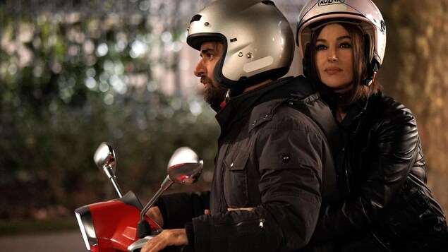 L'actrice porte un casque et est assise derrière un homme sur un scooter. L'actrice porte un casque et est assise derrière un homme sur un scooter.