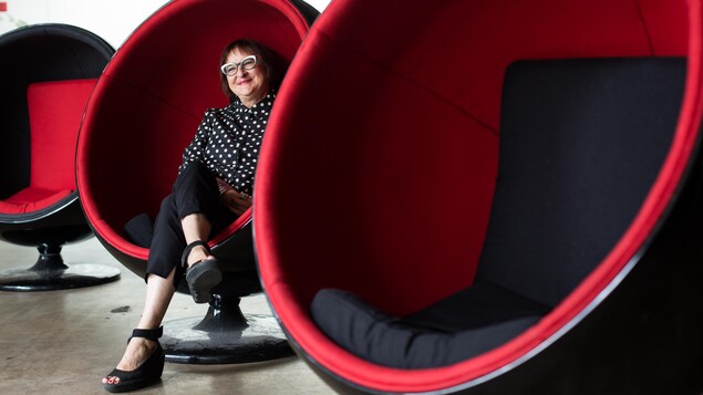 Une photo de Monique Savoie assise dans une chaise en forme de sphère. Une photo de Monique Savoie assise dans une chaise en forme de sphère.