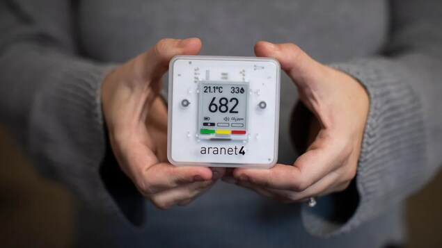 Une personne tient dans ses mains le détecteur de dioxyde de carbone de la compagnie Aranet indiquant 682 ppm.