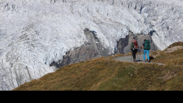 Deux personnes marchent sur une partie gazonnée en direction d'un immense glacier. 