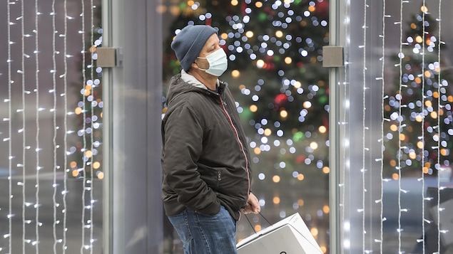 Un homme masqué marche devant un commerce illuminé.