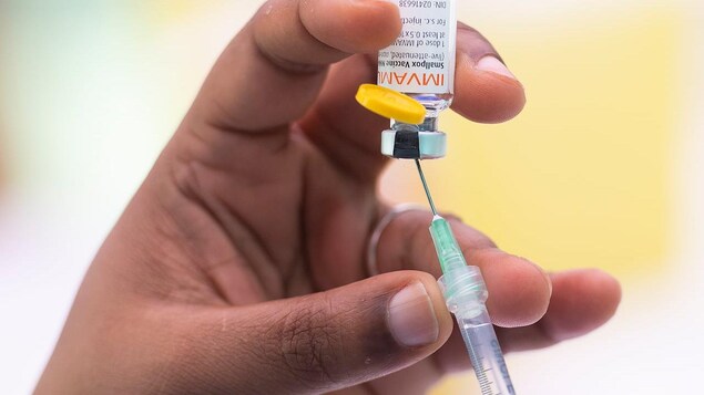 Two hands are filling up a syringe in a vaccine vial.