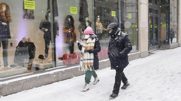 Des passants marchent au centre-ville de Montréal sous la neige, portant un couvre-visage.