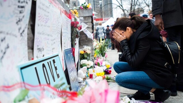 Une femme est accroupie devant des messages et des fleurs.