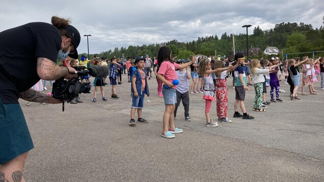Un adulte filme des enfants qui dansent dans une cour d'école.