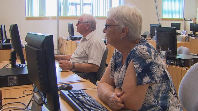 Deux aînés assis devant des ordinateurs écoutent les explications du formateur.