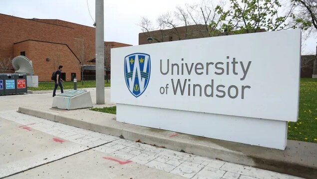 Un panneau de l'Université de Windsor avec un étudiant qui marche au loin.