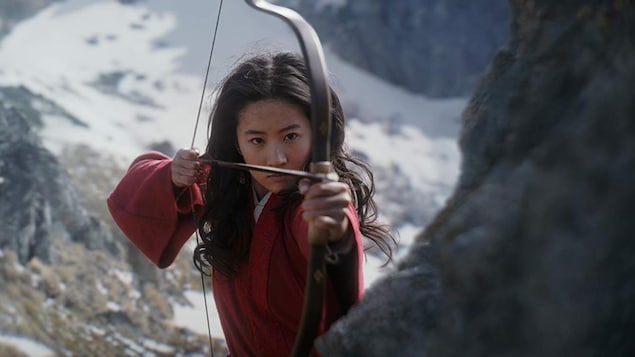 Une femme vêtue d'une tenue rouge tend la corde d'un arc à flèche.