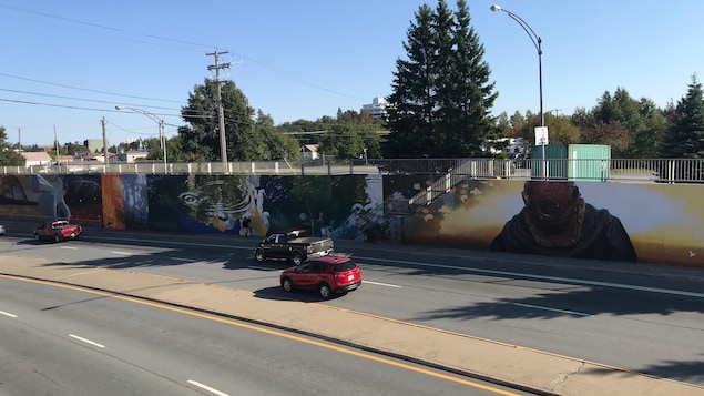Une murale est peinte sur le mur d'un viaduc, où circulent des voitures. Une murale est peinte sur le mur d'un viaduc, où circulent des voitures.