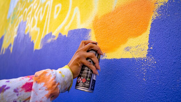 Une main tient une bonbonne de peinture pour appliquer de la couleur sur un mur. 