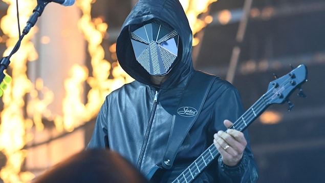Un guitariste performe en étant vêtu d'un manteau, d'un capuchon et d'un masque métallique. 