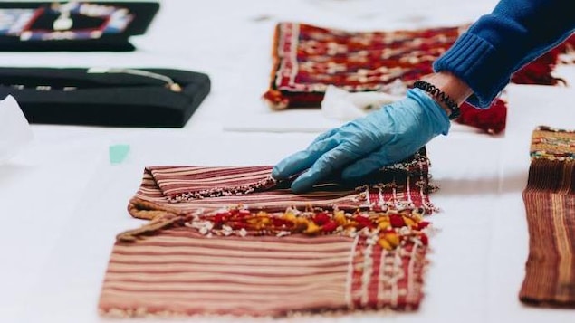 Un.a técnico.a examina textiles antiguos con guantes azules.
Un.e technicien.ne examine des textiles anciens avec des gants bleus.