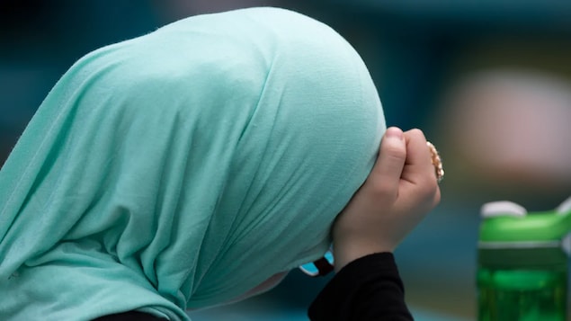 Une femme de dos, elle porte le voile et a la tête penchée.