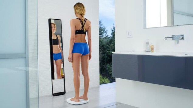 Une femme se pèse devant un miroir de plain-pied. Une femme se pèse devant un miroir de plain-pied.