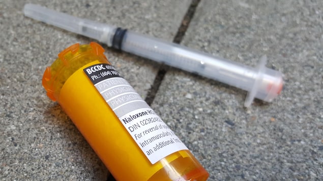 Une seringue usée et un flacon ouvert sur lequel est apposé une ordonnance pour naloxone sont sur le pavé. Une seringue usée et un flacon ouvert sur lequel est apposé une ordonnance pour naloxone sont sur le pavé.