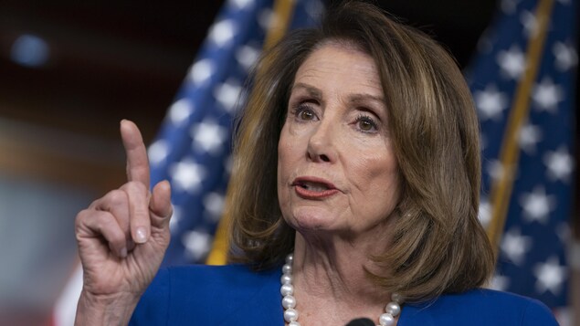 Nancy Pelosi est au micro avec le drapeau américain en toile de fond.