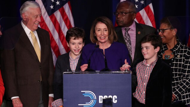 Nancy Pelosi, souriante, derrière un podium, entourée de quelques personnes, dont deux enfants. Nancy Pelosi, souriante, derrière un podium, entourée de quelques personnes, dont deux enfants.