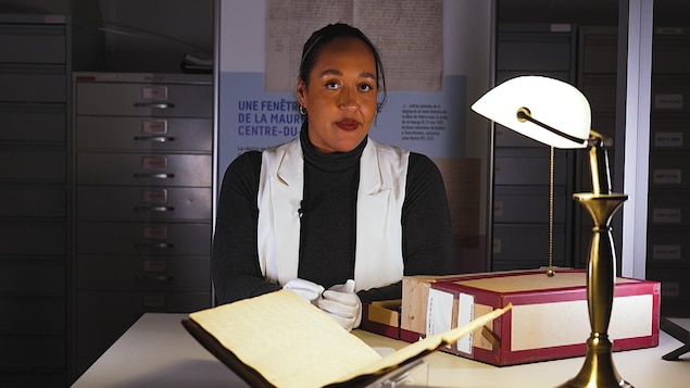 La journaliste Naomie Duckett Zamor entourée de documents d'archives.