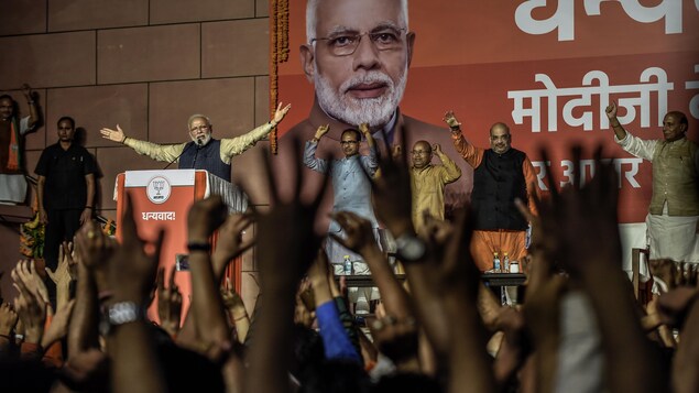Une foule acclame M. Modi qui lève les bras en signe de victoire.