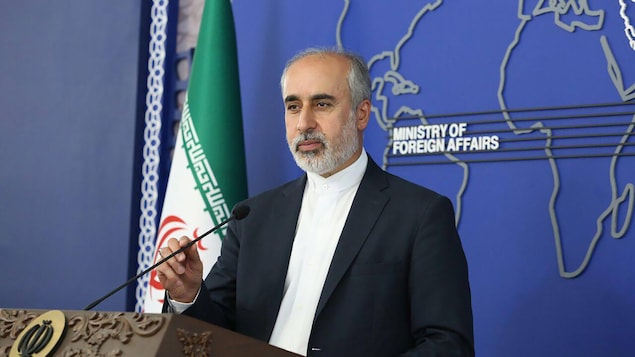 Nasser Kanani en conférence de presse à côté d'un drapeau iranien