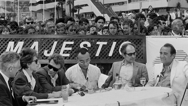 Nathalie Baye, Johnny Hallyday, Jean-Luc Godard et Claude Brasseur sont assis à une table, observés par le public, lors du Festival de Cannes de 1985. Nathalie Baye, Johnny Hallyday, Jean-Luc Godard et Claude Brasseur sont assis à une table, observés par le public, lors du Festival de Cannes de 1985.