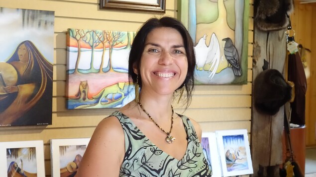 Une femme sourit devant des tableaux d'arts autochtones