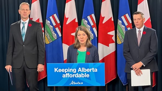 La première ministre de l'alberta, Danielle Smith, parle devant un pupitre, entourée de deux des ministres de son gouvernement, le 1er novembre 2023 à l'Assemblée législative de l'Alberta.