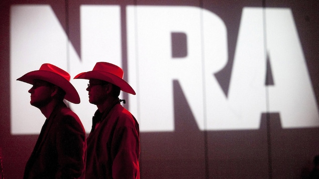 Deux cowboys se tiennent debout devant une projection des lettres NRA.
