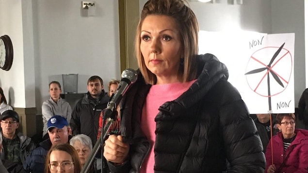 Une femme debout devant un micro lors d'une assemblée publique.