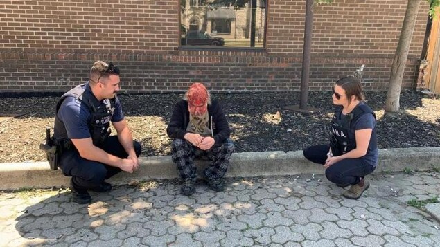 Deux policiers interviennent auprès d'une personne qui est assise sur le trottoir.