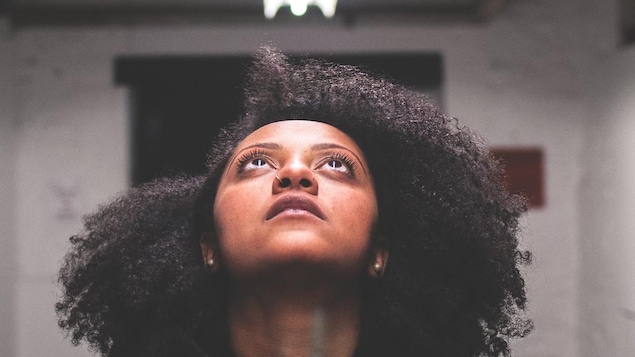 Portrait de la rappeuse Naya Ali, qui regarde vers un néon au plafond.