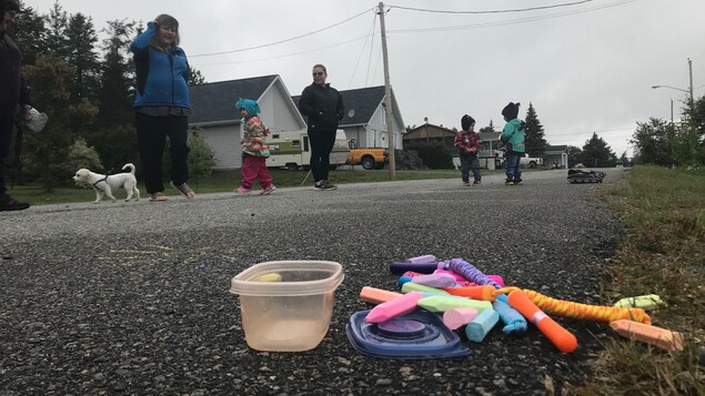 Des enfants et des mamans jouent dans la rue, des craies de marelle posées au sol.