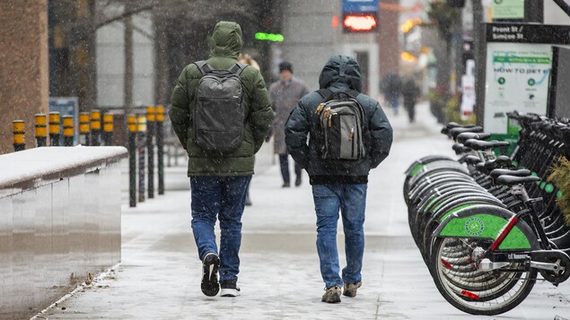 Deux hommes marchent sur une rue du centre-ville sous la neige.