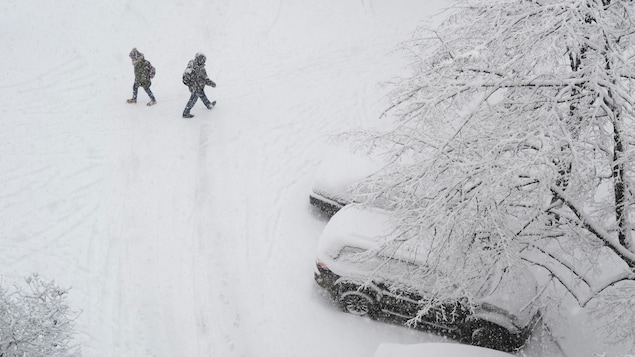 Des piétons devant des voitures enneigées pendant une tempête de neige.