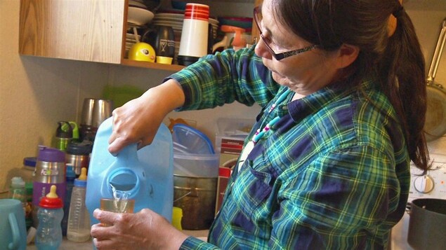 Une Autochtone se verse un verre d'eau embouteillée.