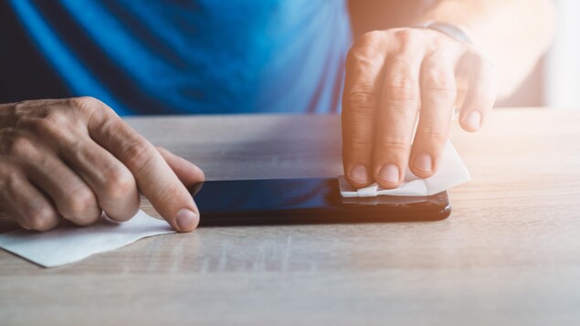 Une homme nettoie l'écran d'un téléphone intelligent avec une lingette.