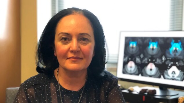 Une femme pose pour la photo avec un écran d'imagerie de cerveau en arrière-fond.