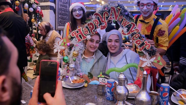Two young women are posing for a picture as two clowns hold a 'Happy New Year' banner above their heads in a restaurant in Cairo.
