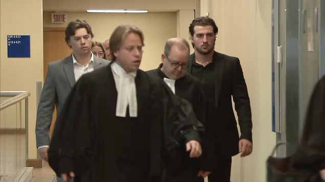 Daigle est vêtu d'un complet gris pâle alors que Siciliano porte un complet noir.  Ils marchent derrière leurs avocats.
