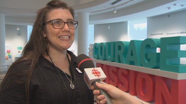 Une femme répond à une question non loin de la reproduction des mots courage en turquoise et passion en rouge. Une femme répond à une question non loin de la reproduction des mots courage en turquoise et passion en rouge.