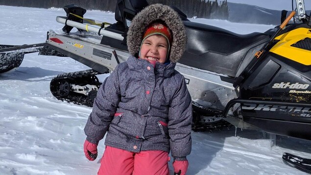 Une petite fille à genoux sur la neige posant devant sa prise de poisson pendant une séance de pêche sur la glace
