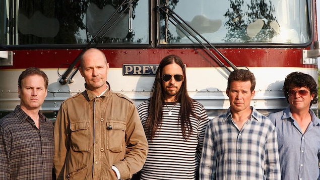 Les cinq membres du groupe posent devant un bus