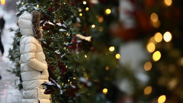 Une femme qui porte un manteau d'hiver regarde des arbres décorés pour Noël.