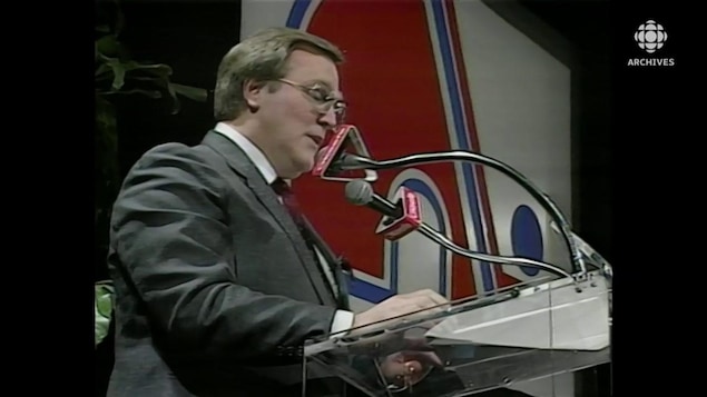 Marcel Aubut, en conférence de presse. Le logo des Nordiques trône en arrière-plan.