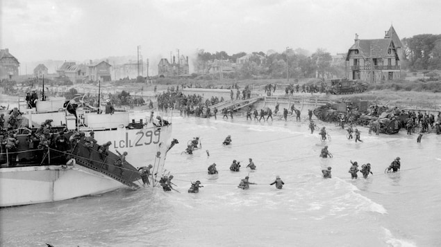 Une photo d'archives en noir et blanc montre des soldats qui débarquent de bateaux sur une plage.