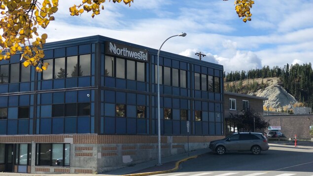 Le bâtiment de deux étages de Northwestel à Whitehorse avec une voiture garée devant et des arbres aux feuilles automnales.